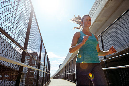 Im strict with my exercise routine. a sporty young woman running on a footbridge.の写真素材