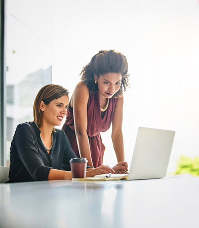 In it to achieve a high level of success together. two businesswomen working together on a laptop in an office.の写真素材