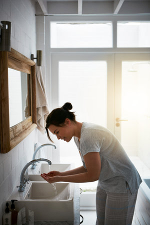 Thatll wake you right up. an attractive young woman washing in the bathroom.の写真素材