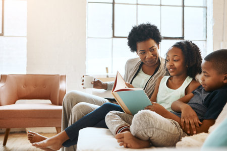 Children benefit the most from reading. a little brother and sister reading a book while their mother watches at home.の写真素材