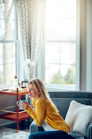 Staying home was a good idea. a young woman relaxing on her sofa with a cup of coffee.の写真素材