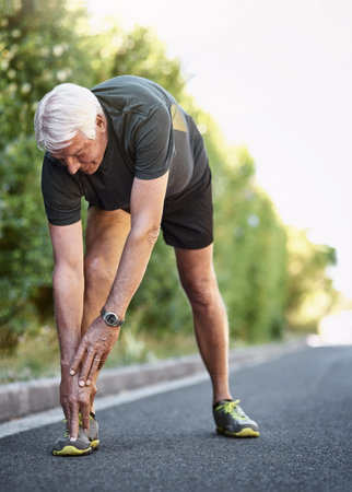 Getting a good warmup is vital for a great workout. a senior man warming up before a run outside.