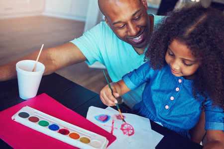 Which color is your favorite. a cute little girl and her father painting together at the kitchen table.の写真素材