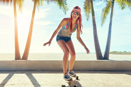 Take adventure into your own hands. a young woman hanging out on the boardwalk with her skateboard.の写真素材