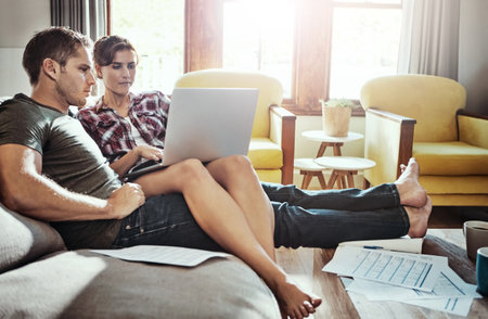 Great financial planning afforded them this comfortable lifestyle. a young couple using a laptop and going through paperwork together on the sofa at home.の写真素材