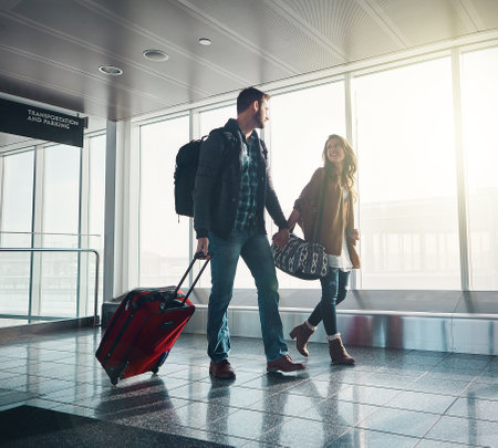 Its goodbye for now but not forever. a young couple walking in an airport with their luggage while holding hands and looking at one another.の写真素材