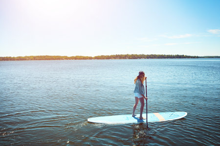 Setting off to discover the waters. an attractive young woman paddle boarding on a lake.の写真素材