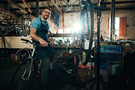 Allow me to take care of all your bicycle needs. Portrait of a mature man working in a bicycle repair shop.の写真素材
