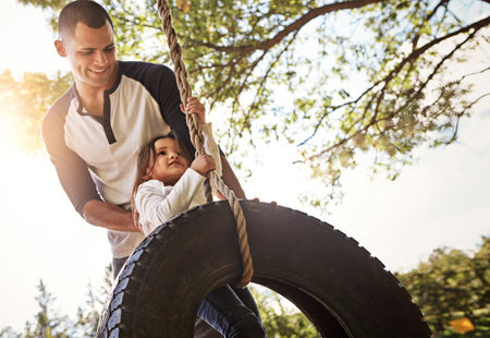 Hold on tight. a happy father pushing his daughter on a tyre swing.の写真素材