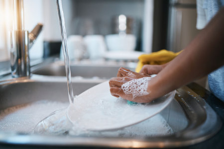 Hands, sink and cleaning dishes with a person in the kitchen of a home to wash a plate for hygiene. Water, bacteria and soap with an adult washing porcelain crockery in a house to clean for houseworkの写真素材