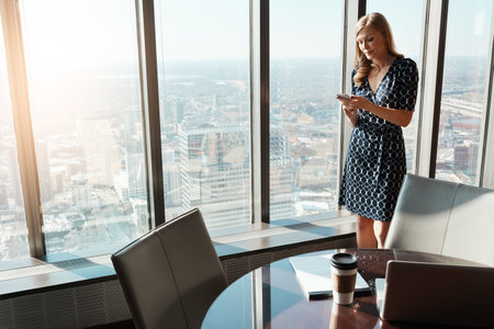 Managing business straight from her smartphone. a young businesswoman using a cellphone in an office.の写真素材
