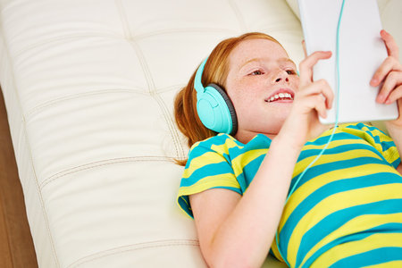 lnteractive screen time makes learning a breeze. a little girl using a digital tablet with headphones at home.の写真素材