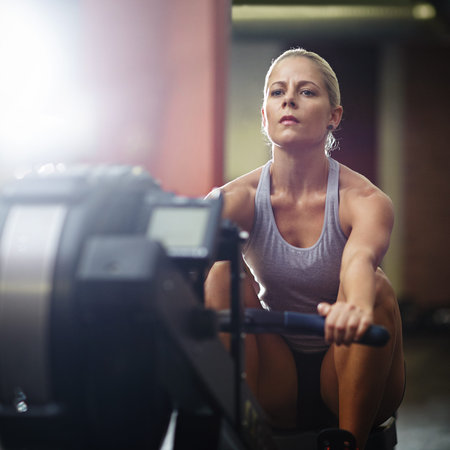 Turn your sweat into results. a young woman working out on a rowing machine in a gym.