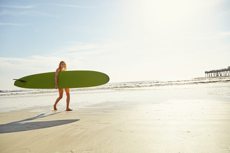 Shes got a passion for surfing. an attractive young woman carrying her surfboard on the beach.