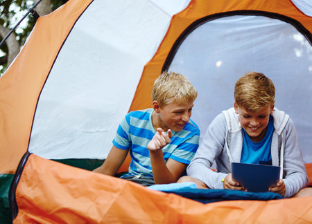 Always connected, no matter where they are. two young boys using a digital tablet while in their tent.の写真素材