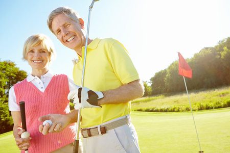 Golf keeps us bonding regularly. Elderly couple holding their golf clubs and balls on the green.の写真素材