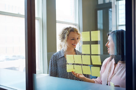 Theyre on to something good. two businesswomen brainstorming with adhesive notes on a glass wall in an office.の写真素材