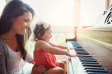 Piano lessons with Mom are always fun. a mother watching her adorable little daughter playing the piano at home.の写真素材