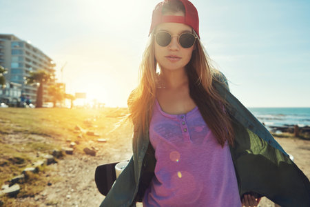Summers better on a skateboard. a young woman hanging out on the boardwalk with her skateboard.の写真素材