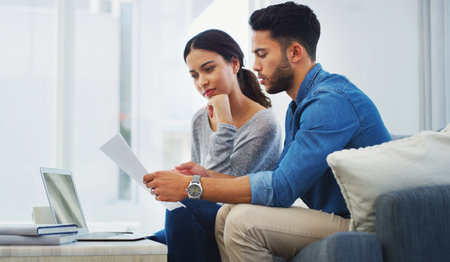 Whats the best way to save. a young couple sitting on the sofa while going through paperwork in their lounge.の写真素材