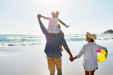 Two of lifes best, family and summer. an adorable little girl going for a walk with her parents on the beach.の写真素材