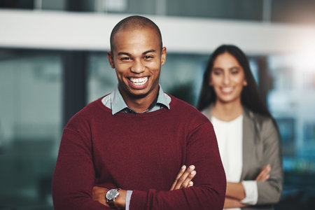 Youll go far as long as you have confidence. Portrait of a young businessman standing in an office with his colleague in the background.の写真素材
