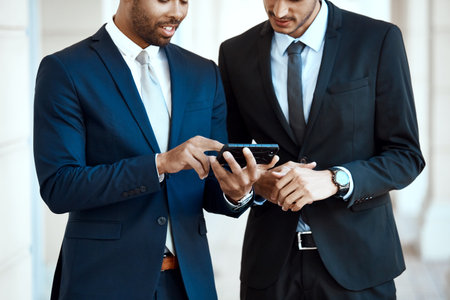 Cellphones are so convenient in the city. unrecognizable businessmen using a cellphone together outside.の写真素材