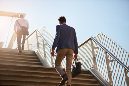 All on our way to the office. Low angle shot of unrecognizable businessmen walking up stairs outside.の写真素材