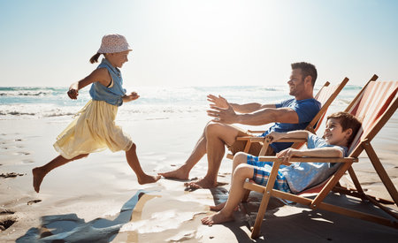 Making it a day of carefree fun in the sun. a little girl running towards her father and brother at the beach.の写真素材