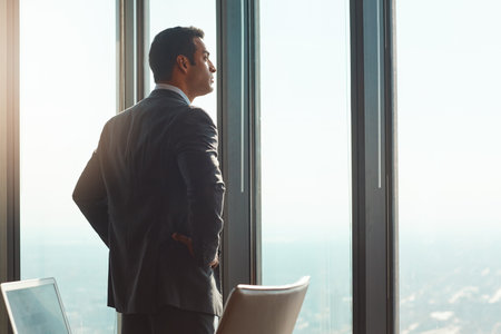 He made it to the top. Rearview shot of a handsome young businessman standing with his hands on his hips in the office.の写真素材