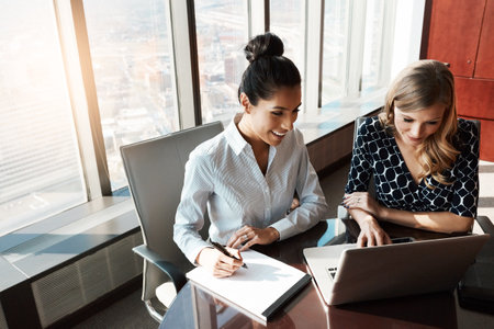 Time to tackle their new team project together. two businesswomen working together on a laptop in an office.の写真素材