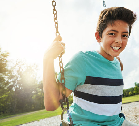Making it a day filled with endless joy. Portrait of a young boy playing on a swing at the park.の写真素材