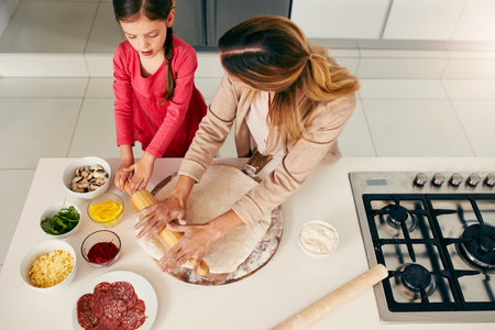 Pizza is everyones favorite. High angle shot of a middle aged mother and her daughter preparing a pizza to go into the oven in the kitchen at home.の写真素材