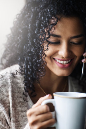 Some nice coffee to keep me awake and smiling. a cheerful young woman relaxing and drinking coffee while talking on her cellphone at home during the day.の写真素材