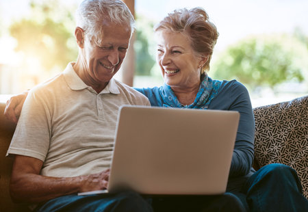 Keeping up with modern times. a happy senior couple using a laptop together on the sofa at home.の写真素材