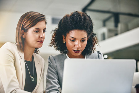 The world online helps lead their ideas to the forefront. two businesswomen working together on a laptop in an office.の写真素材