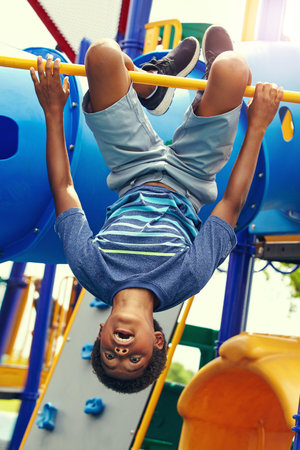 Kids see life differently. a young boy hanging upside down on a jungle gym in the park.の写真素材