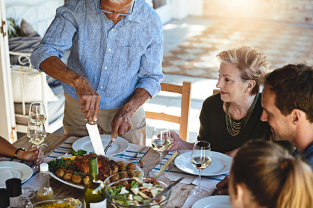 Laid-back luncheons with family. a mature man carving a roast while enjoying lunch with his family outside.の写真素材