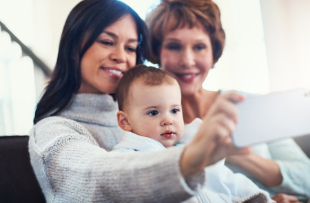 Who needs the boys to take an awesome family selfie. a young woman taking selfies with her baby girl and mother at home.の写真素材