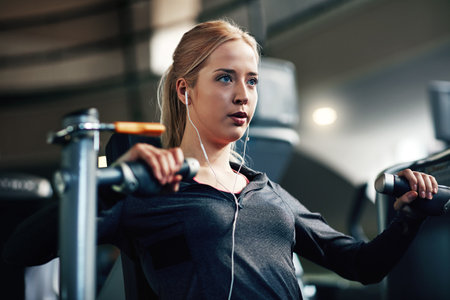 Her fitness game gets stronger with every workout. a young woman working out with a chest press at a gym.の写真素材