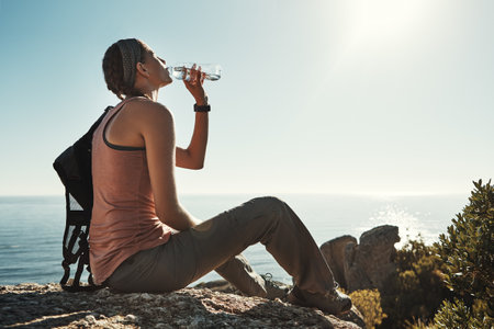 Stopping for a quick sip before continuing her adventure. a young woman drinking water while out on a hike through the mountains.の写真素材