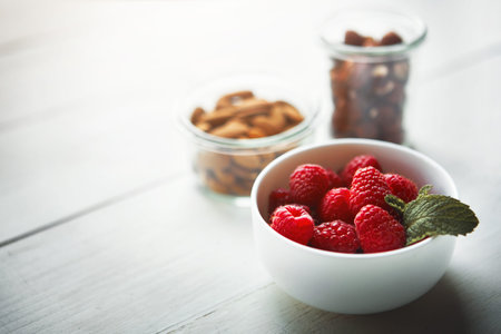 Snacks to slim down with. fresh raspberries in a bowl with nuts blurred in the background.