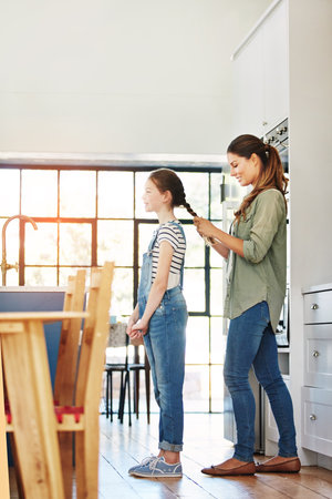 Your hair is growing beautifully. a happy mother braiding her daughters hair at home.の写真素材
