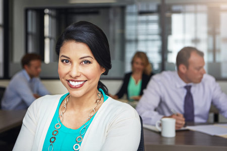 Shes the epitome of job satisfaction. Portrait of a businesswoman working at her desk with her colleagues in the background.の写真素材