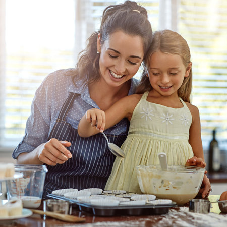Adding a spoonful of love. a mother and her daughter baking in the kitchen.の写真素材