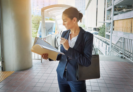 Brushing up on her way to a meeting. a young businesswoman reading paperwork on her way to the office.の写真素材