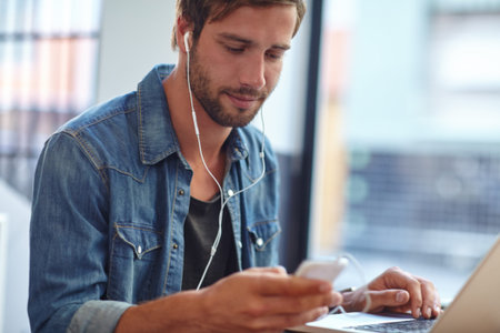 Coffee and music makes him more productive. a young man listening to music while using his laptop at...