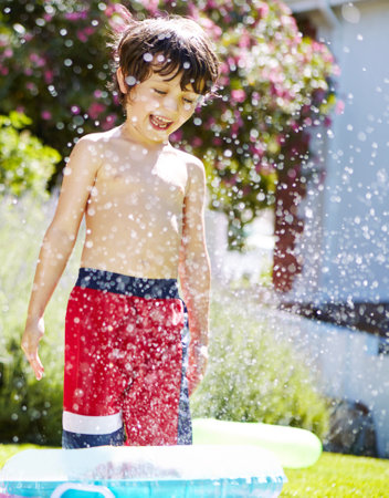 Having a blast in the backyard. a little boy playing outside in the water from the sprinkler.の写真素材