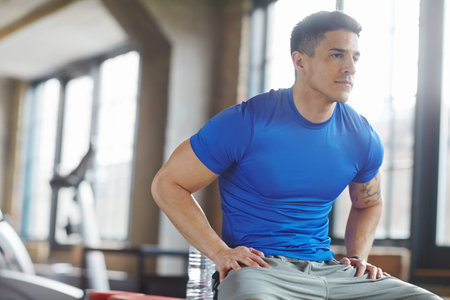 Fit athlete sitting alone in gym and taking break during his workout. Sporty, athletic, active,...