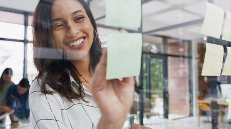 Elevating every idea a bit more. a young businesswoman brainstorming with notes on a glass wall in...